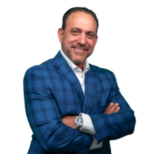 Smiling man in a blue plaid blazer with white shirt, arms crossed toward the camera.